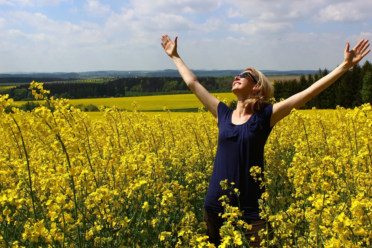 Frau im Rapsfeld mit Hände in den Himmel gestreckt