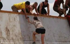 Frau klettert die Mauer nach oben und helfende Hände strecken sich ihr entgegen