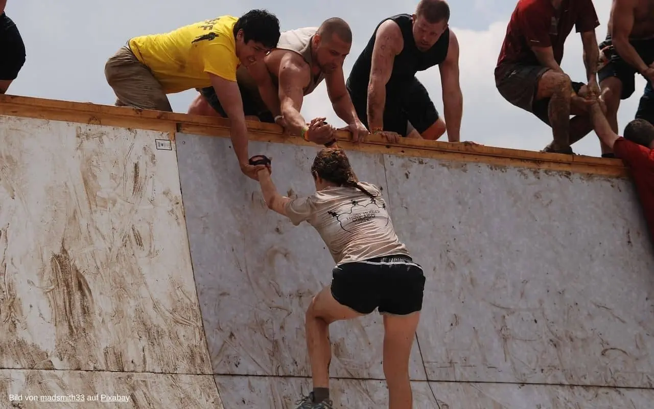 Frau klettert die Mauer nach oben und helfende Hände strecken sich ihr entgegen