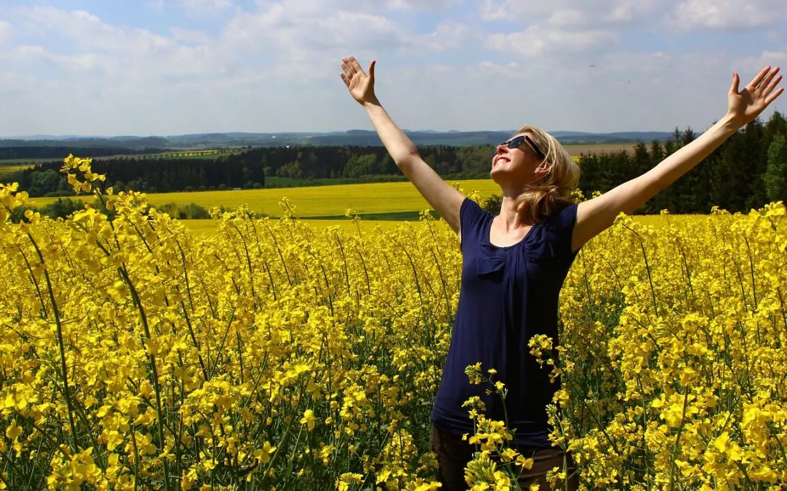 Frau im Rapsfeld mit Hände in den Himmel gestreckt