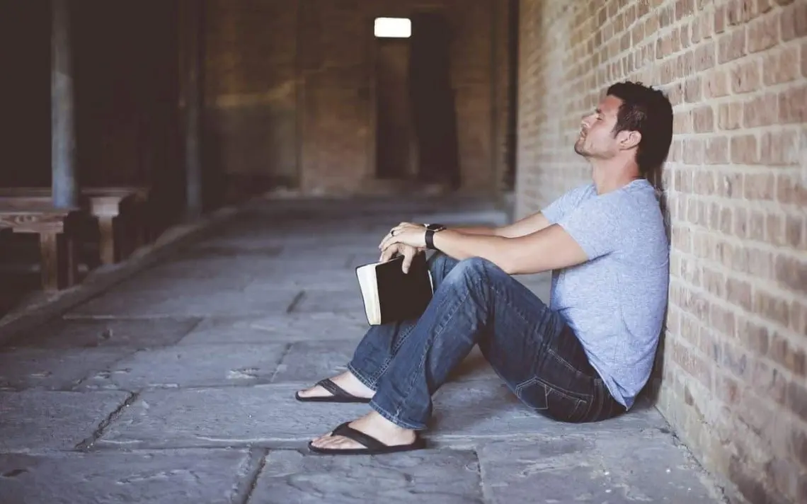 Mann lehnt an der Mauer und hält die Bibel in der Hand